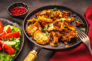 Chanterelle mushrooms fried with potatoes according to a traditional recipe in a cast-iron pan on a dark table with a burgundy napkin, with vegetables and berries