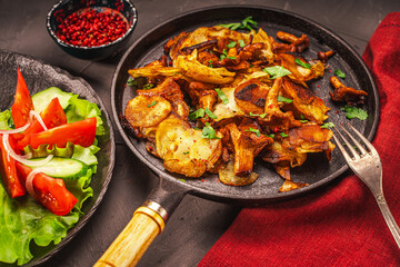 Chanterelle mushrooms fried with potatoes according to a traditional recipe in a cast-iron pan on a dark table with a burgundy napkin, with vegetables and berries