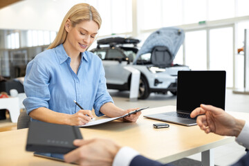 Happy woman signing contract for the purchase of car in showroom