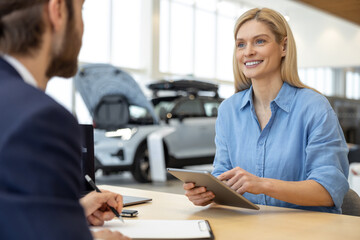 Woman buying new automobile in car showroom signing documents with dealership manager