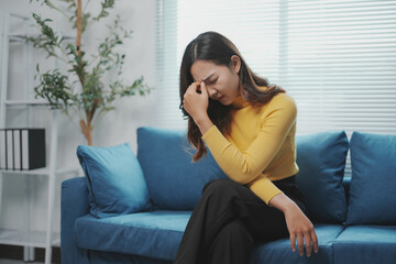 Obraz premium Young businesswoman is feeling sick and having a headache, touching her temples while sitting on a sofa in the living room