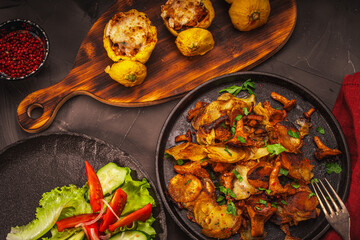 Chanterelle mushrooms fried with potatoes in a cast-iron pan and stuffed pumpkins on a wooden board, vegetables and a burgundy napkin on a gray table. Beautiful presentation of the dish.