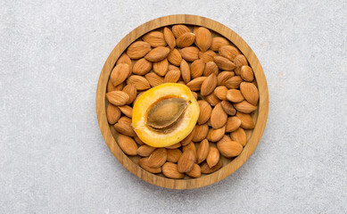 Apricot kernels in a wooden bowl, whole apricots on a light background. Horizontal, close.