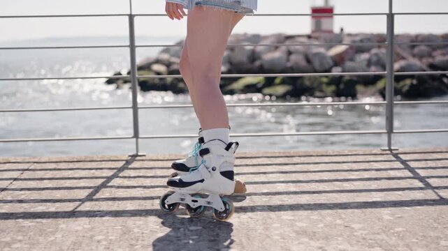 Close-up of a woman's legs roller skating on a sunny boardwalk by the sea, enjoying an outdoor activity.