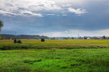 Fototapeta premium A serene green meadow stretches across the horizon, framed by dark clouds and soft light as day transitions to night in the peaceful countryside.