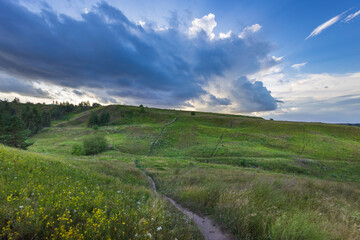 A vibrant expanse of lush green hills stretches beneath an expansive sky filled with dynamic clouds...