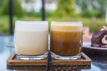 Two glasses of coffee sit on a wooden tray, one of which is brown