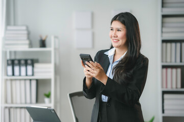 Businesswoman is checking her smartphone and smiling while standing in a modern office