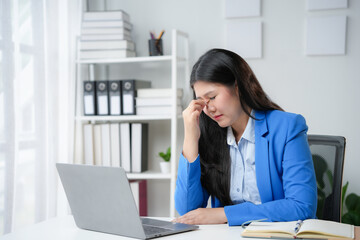 Fototapeta premium Young businesswoman is having a headache and is touching her forehead while sitting in her office