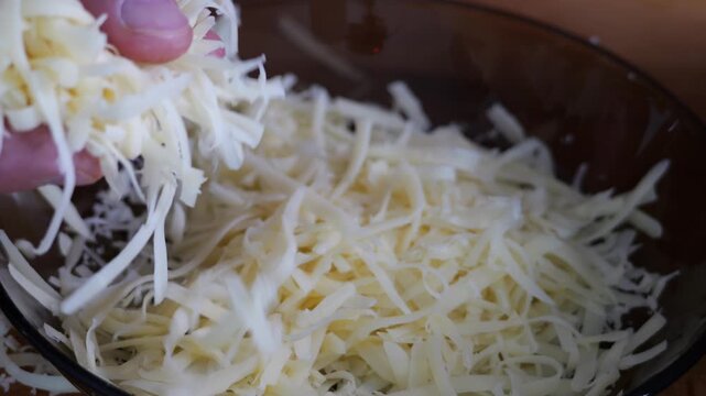 Male hands grating a thick block of cheese on a metal grater, over a wooden table. Preparing family pizza. Natural light in a real kitchen.