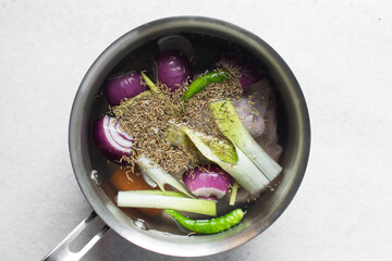 Overhead view of ingredients for making chicken broth in a silver saucepan, top view of raw chicken carrots green chilli spring onions in a saucepan, process of making chicken broth