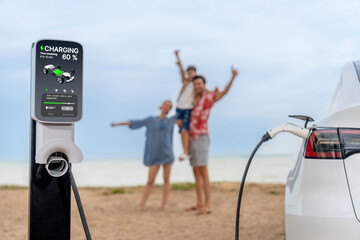 Alternative family vacation trip traveling by the beach with electric car recharging battery from...