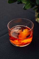 cocktail with ice and orange peel in low rocks glass on black tablecloth