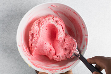 Overhead view of buttercream being colored pink, top view of american buttercream in a white bowl being colored pink, process of making american buttercream