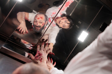 Employees goofing around in office building elevator, dressed as zombies for Halloween corporate...