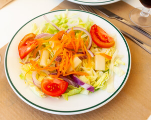 Mediterranean salad with tomato, lettuce and carrot on white plate on wooden table