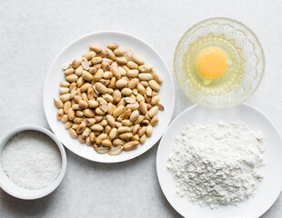 Overhead view of roasted peanuts flour egg and sugar on a marble countertop, flatlay of mise en place of ingredients for making coated peanuts, process of making nigerian coated peanuts