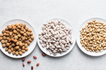 Overhead view of roasted peanuts and coated peanuts on a white plate, flatlay of roasted peeled peanuts and raw coated peanuts on a marble countertop, process of making coated nuts or cracker nuts