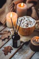 Autumn home perfume in glass bottle with wooden sticks, scented candles as apartment air freshener. Pumpkin sweet latte fragrance, spices, cinnamon, anise. Aromatherapy, cozy atmosphere, comfort