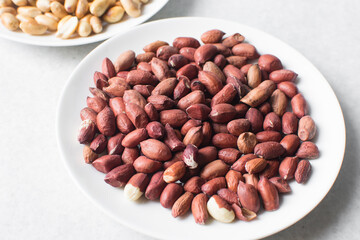 Overhead view of unpeeled raw peanuts on a white plate, flatlay of raw peanuts on a marble countertop, process of making roasted peanuts