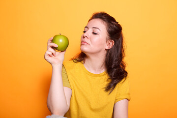 Young woman holding an apple in her hand while being photographed in studio against isolated background. Lady advocating a healthy way of living. Taking fruits for skin care.