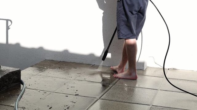 A young man washes garden tiles in his yard using a Karcher.