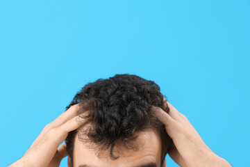 Young brunette man with stylish hairdo on blue background, closeup