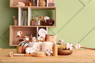Set of cosmetic products, bath supplies and cotton branch on wooden table near color wall