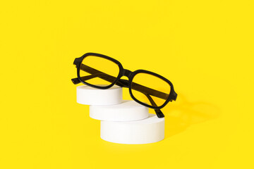 Podium with stylish sunglasses on yellow background