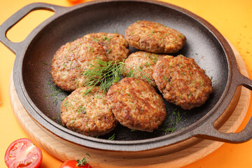Frying pan with cutlets, dill and tomatoes on yellow background