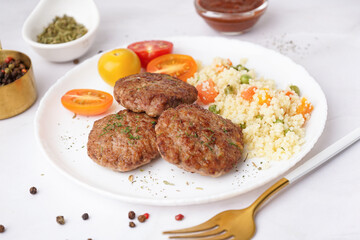 Cutlets with bulgur, boiled vegetables and tomatoes on white table in kitchen