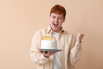 Surprised young man with birthday cake on beige background