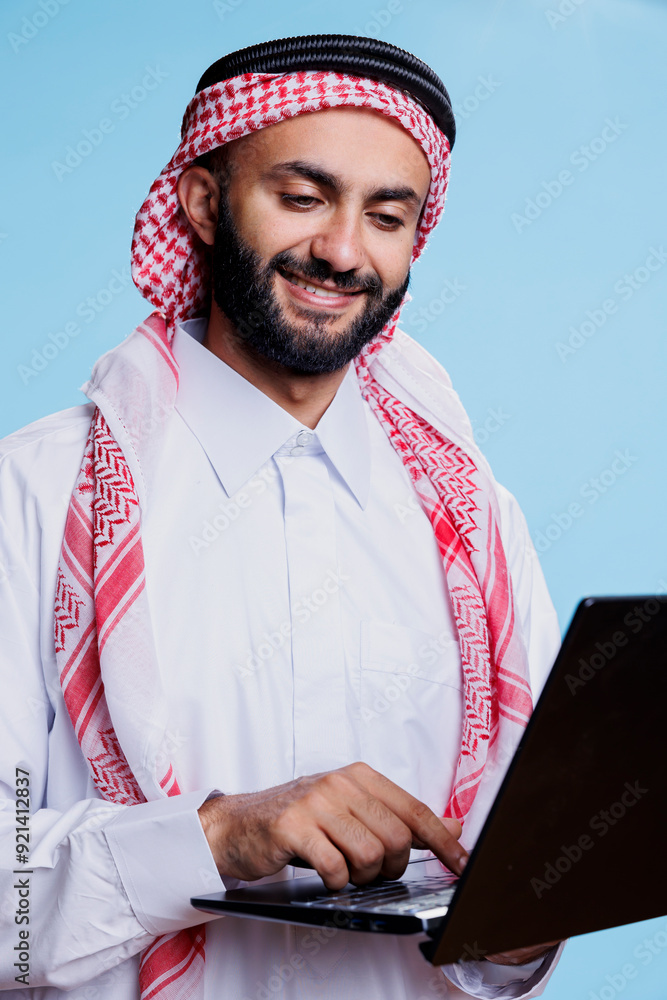Poster smiling muslim man holding laptop and pressing button on keyboard with cheerful expression. arab per