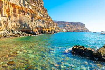 The rocky coastline and cliffs along the Atlantic Ocean at the Playa de Mogan beach in resort town...