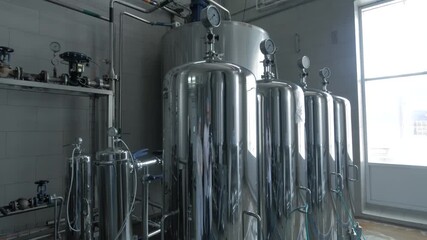 Stainless steel tanks in beverage manufacturing plant. Industrial equipment for liquid storage in modern production facility. Food processing and storage technology in factory environment.