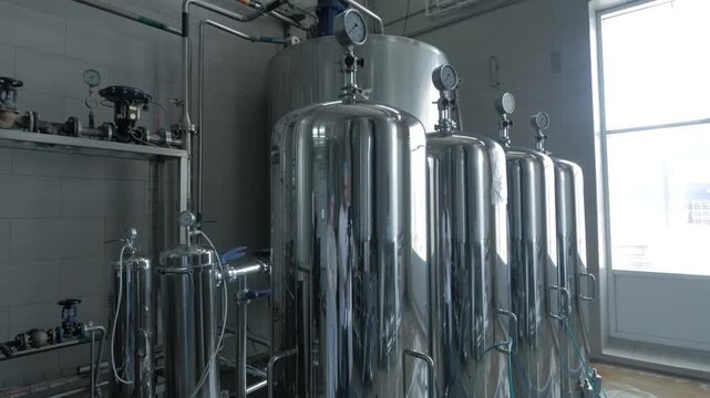 Stainless steel tanks in beverage manufacturing plant. Industrial equipment for liquid storage in modern production facility. Food processing and storage technology in factory environment.