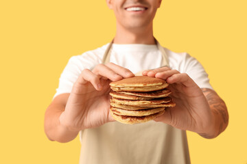 Young man with tasty homemade pancakes on yellow background, closeup