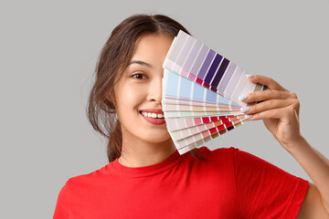 Beautiful young woman with covering face with different palette samples on grey background, closeup