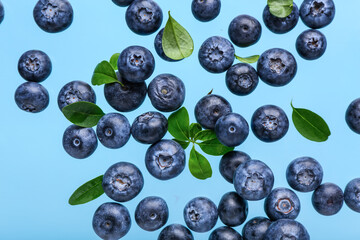 Flying sweet fresh blueberries and leaves on blue background