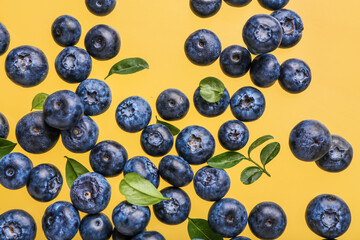 Flying sweet fresh blueberries and leaves on yellow background