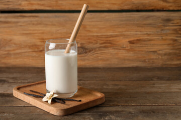 Glass of fresh vanilla milk with sticks and flower on wooden background