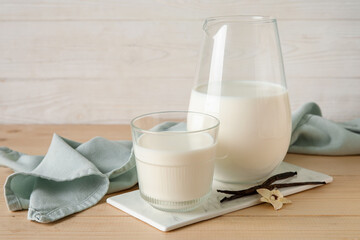 Glass and jug of fresh vanilla milk with sticks and flower on wooden table
