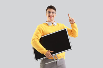 Young man with computer monitor pointing at something on light background