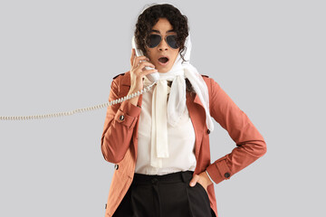 Shocked female African-American spy talking by phone on light background