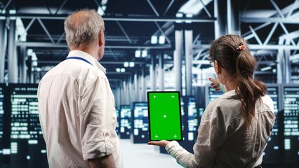 Experts using chroma key tablet to monitor energy efficient data center clusters. Server devices using renewable sources employed to minimize consumption and reduce overall workspace carbon footprint