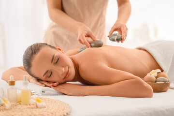 Young woman having massage with hot stones in spa salon