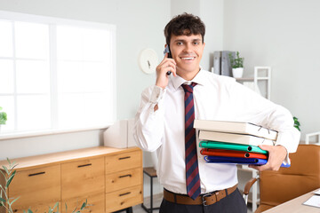 Fototapeta premium Male accountant talking with mobile phone and holding stack of folders in office