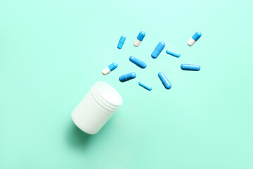 Bottle with flying blue capsules on turquoise background. Top view