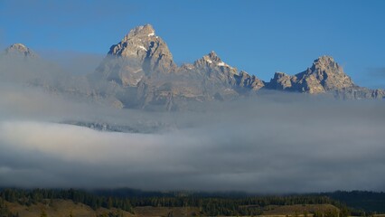 Grand Teton mountain range with low-lying clouds and a clear blue sky in Teton County, Wyoming, USA