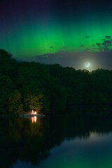 Vertical view of a night landscape with a campfire by a lake, under a green aurora borealis